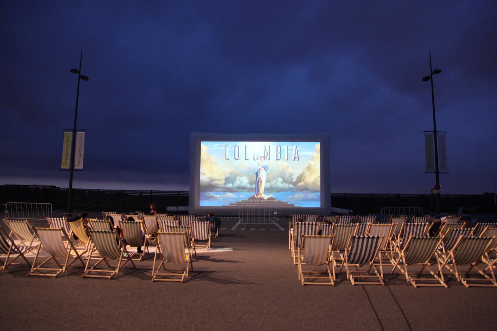 Gigantesco schermo cinematografico gonfiabile Hallucine installato all'aperto, con sedie a sdraio disposte di fronte allo schermo al calar del sole