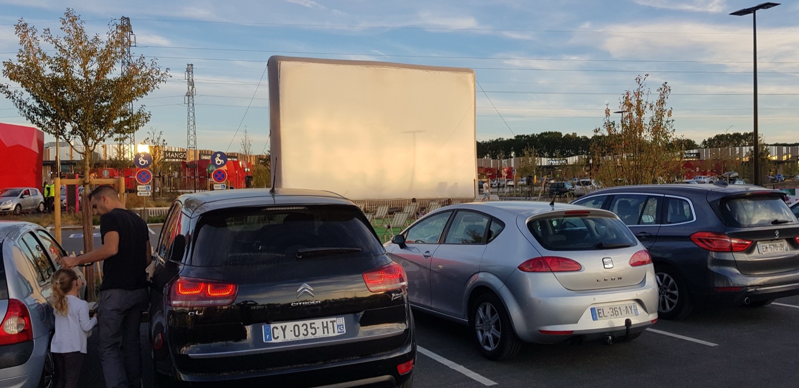 Schermo cinematografico gonfiabile gigante Hallucine installato all'aperto, con auto parcheggiate nelle vicinanze